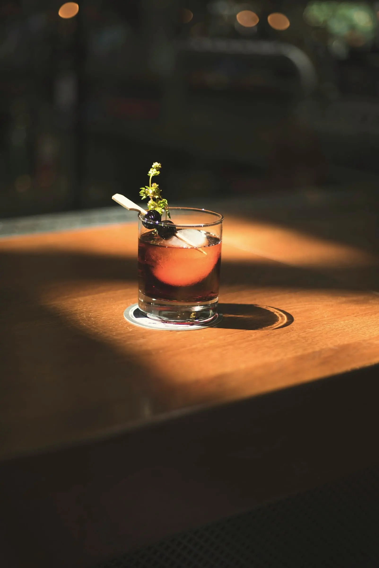 Dark red drink with a herb sprig in a pool of low sun on a wooden table