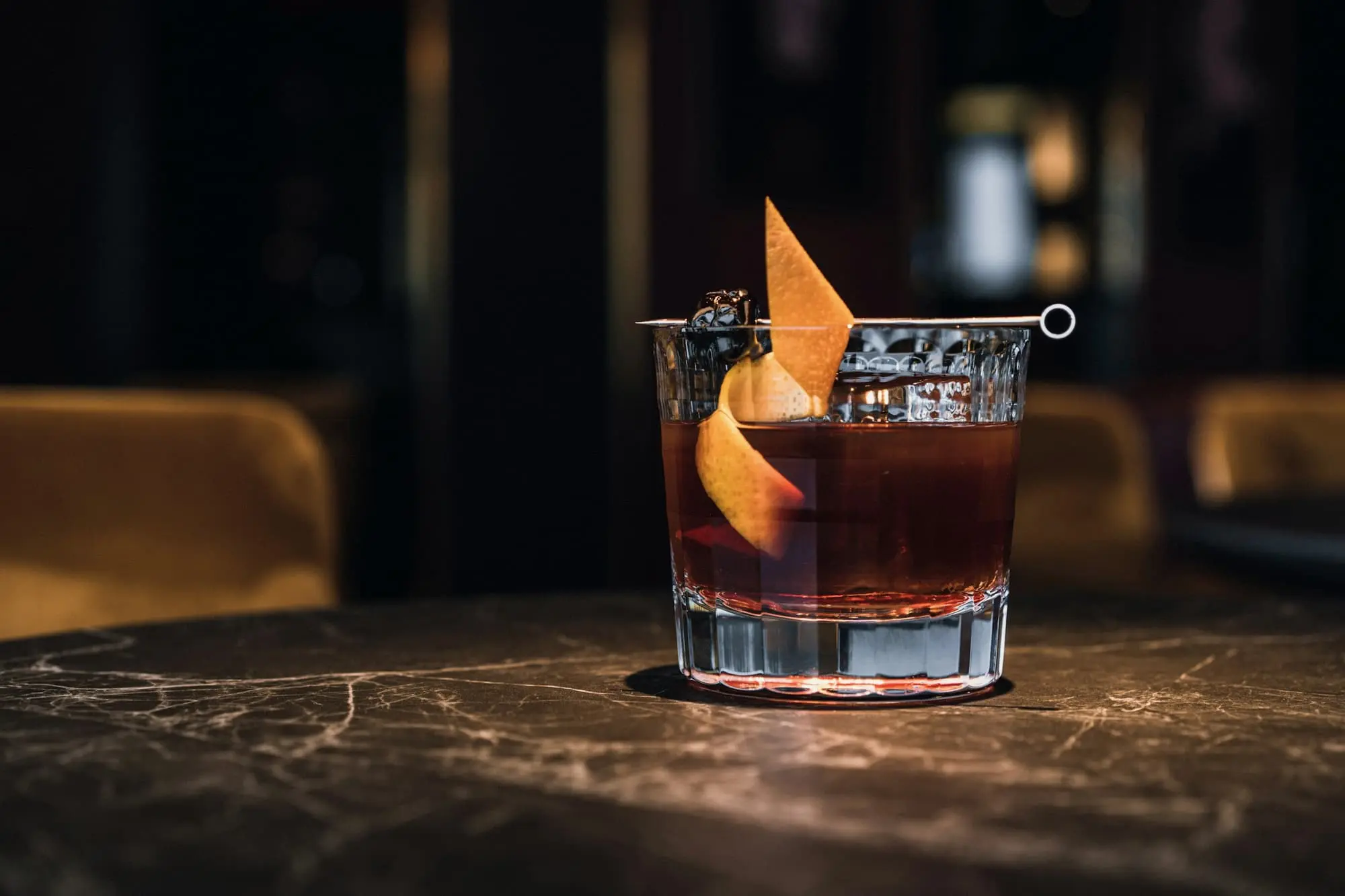 Old fashioned with an orange peel on a veined stone table in a dim room
