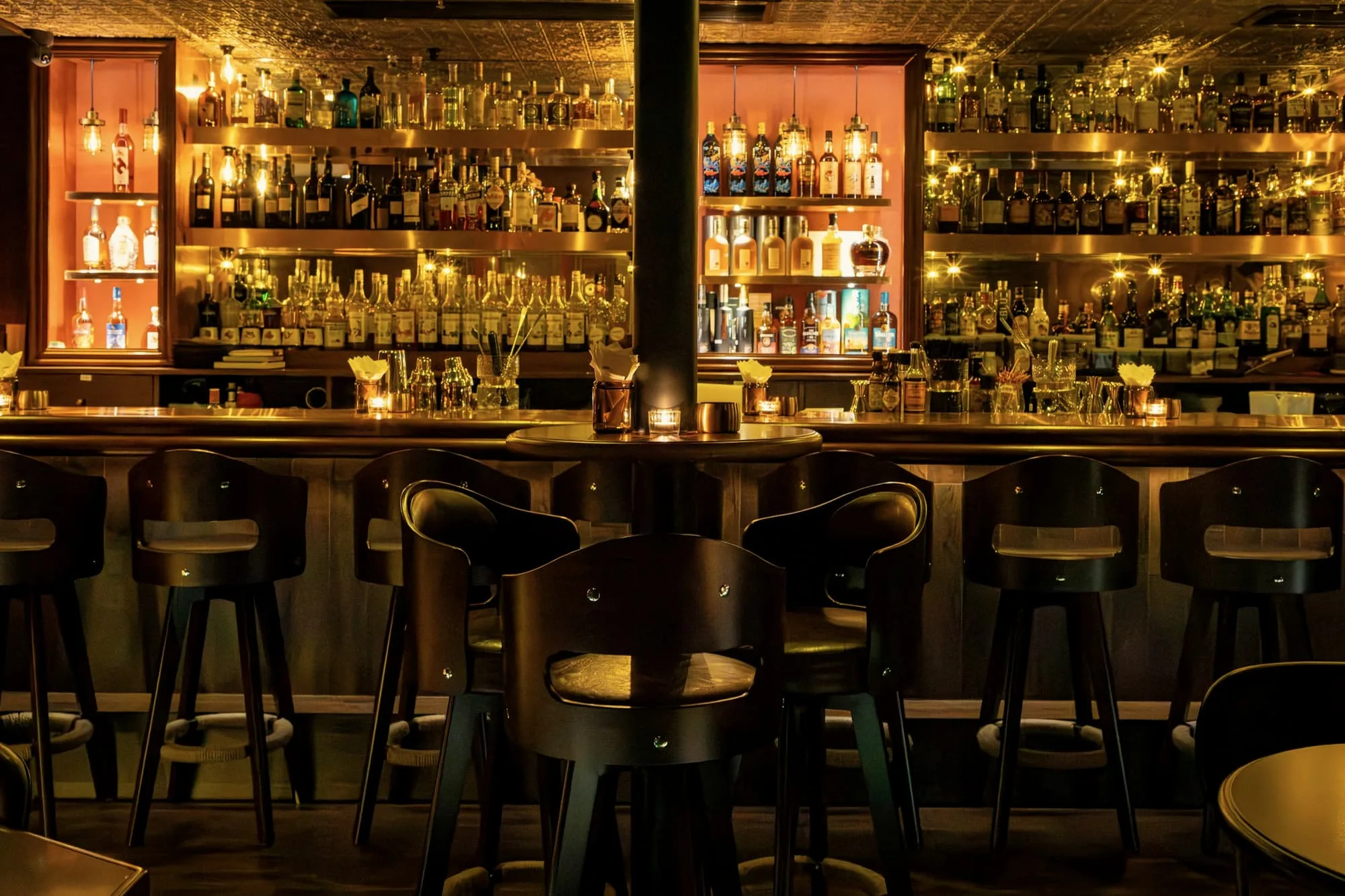 Long bar with low stools before lit shelves of bottles glowing amber