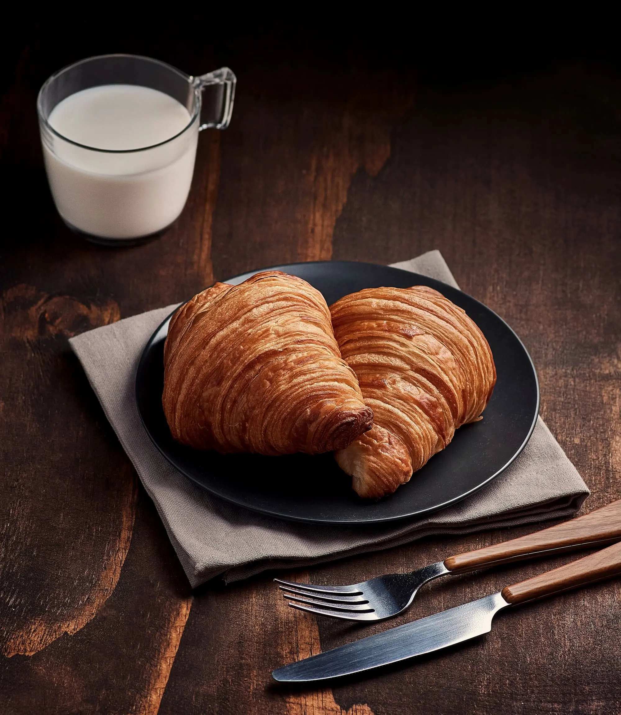 Two croissants on a dark plate over a linen napkin on an old wooden table