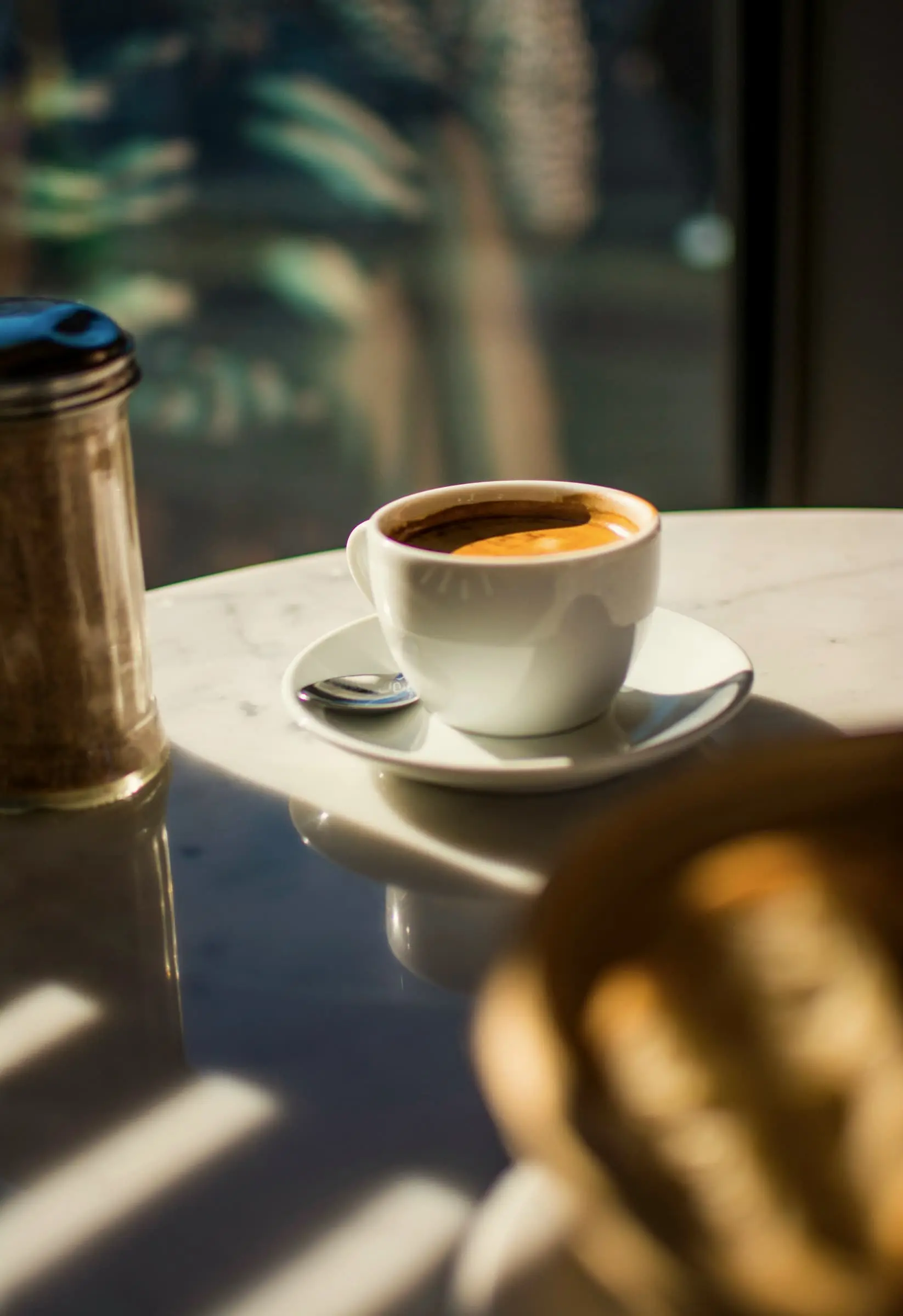 An espresso on a saucer in low morning sun on a marble table