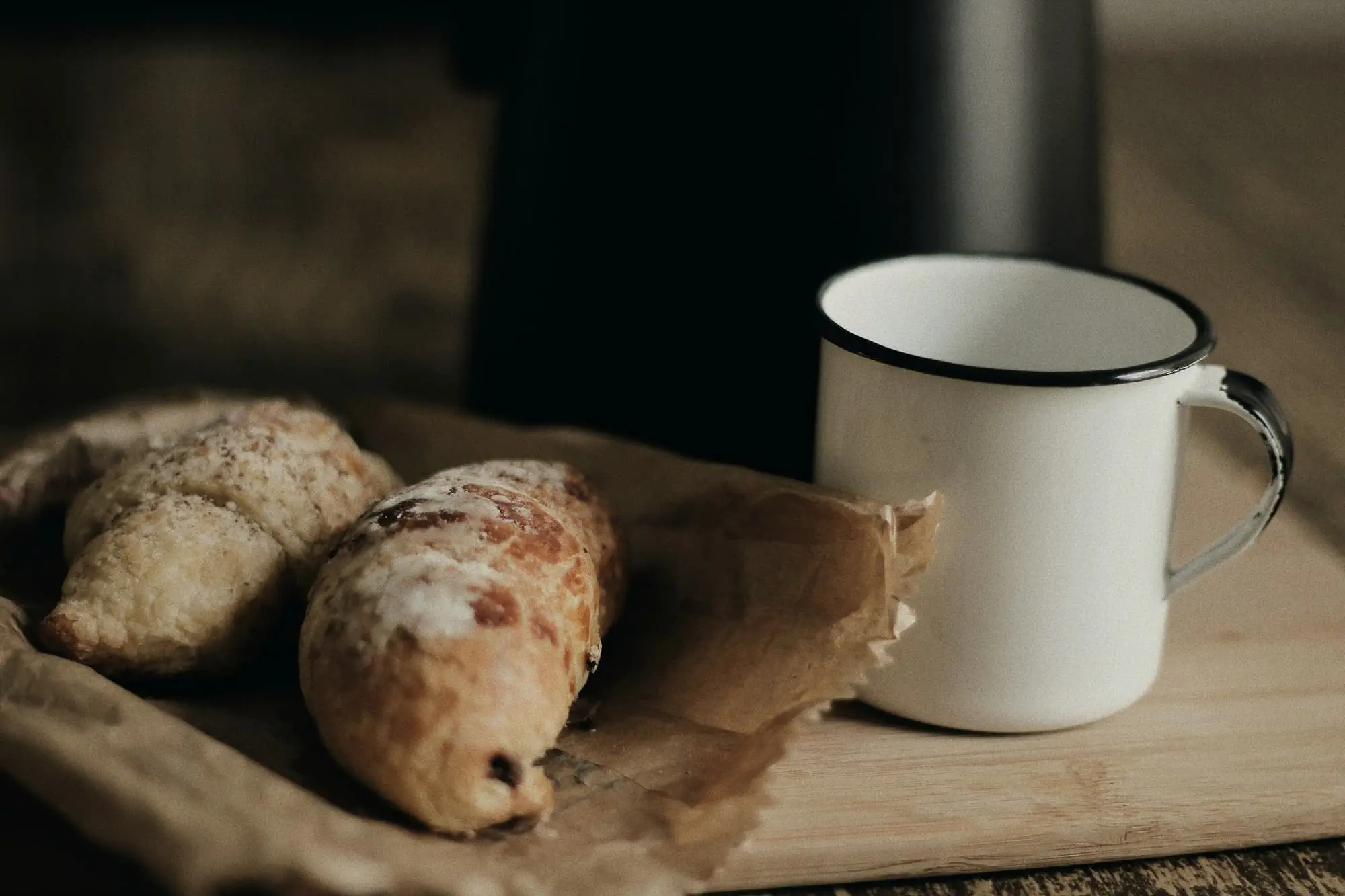 Two seeded rolls on brown paper beside a white enamel mug