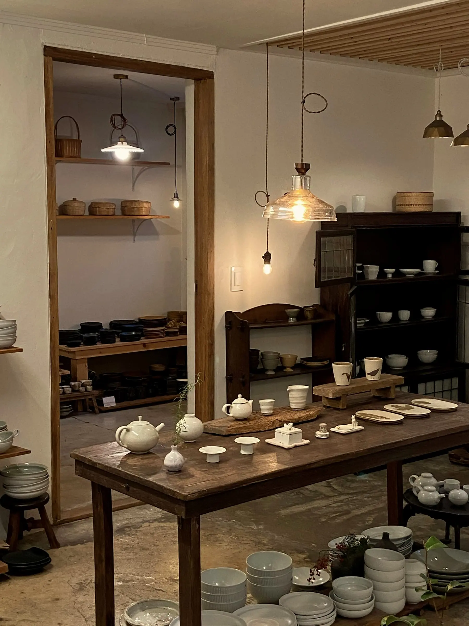A small pottery shop with a wooden table of white ceramics under hanging lamps