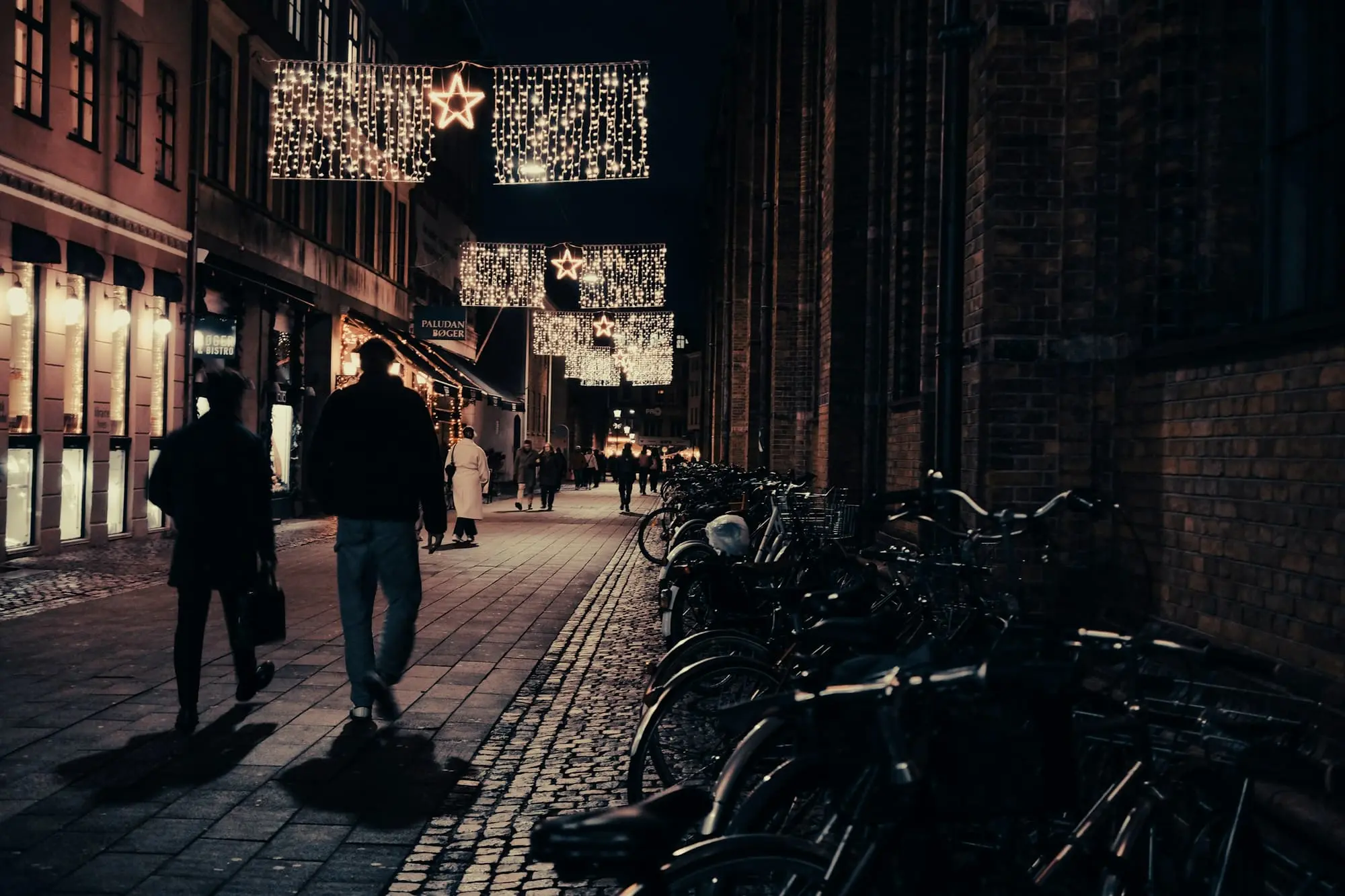 Two people walking a brick lane at night past a row of parked bicycles