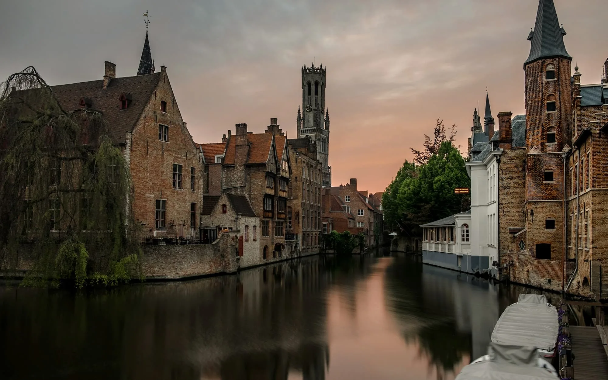 Gabled houses and a belfry reflected in a still canal at dusk