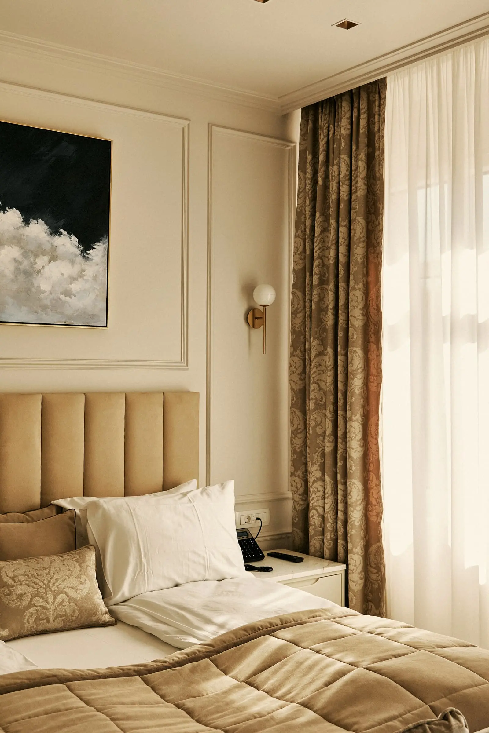 A bed with a soft ribbed headboard against pale panelling beside gold curtains