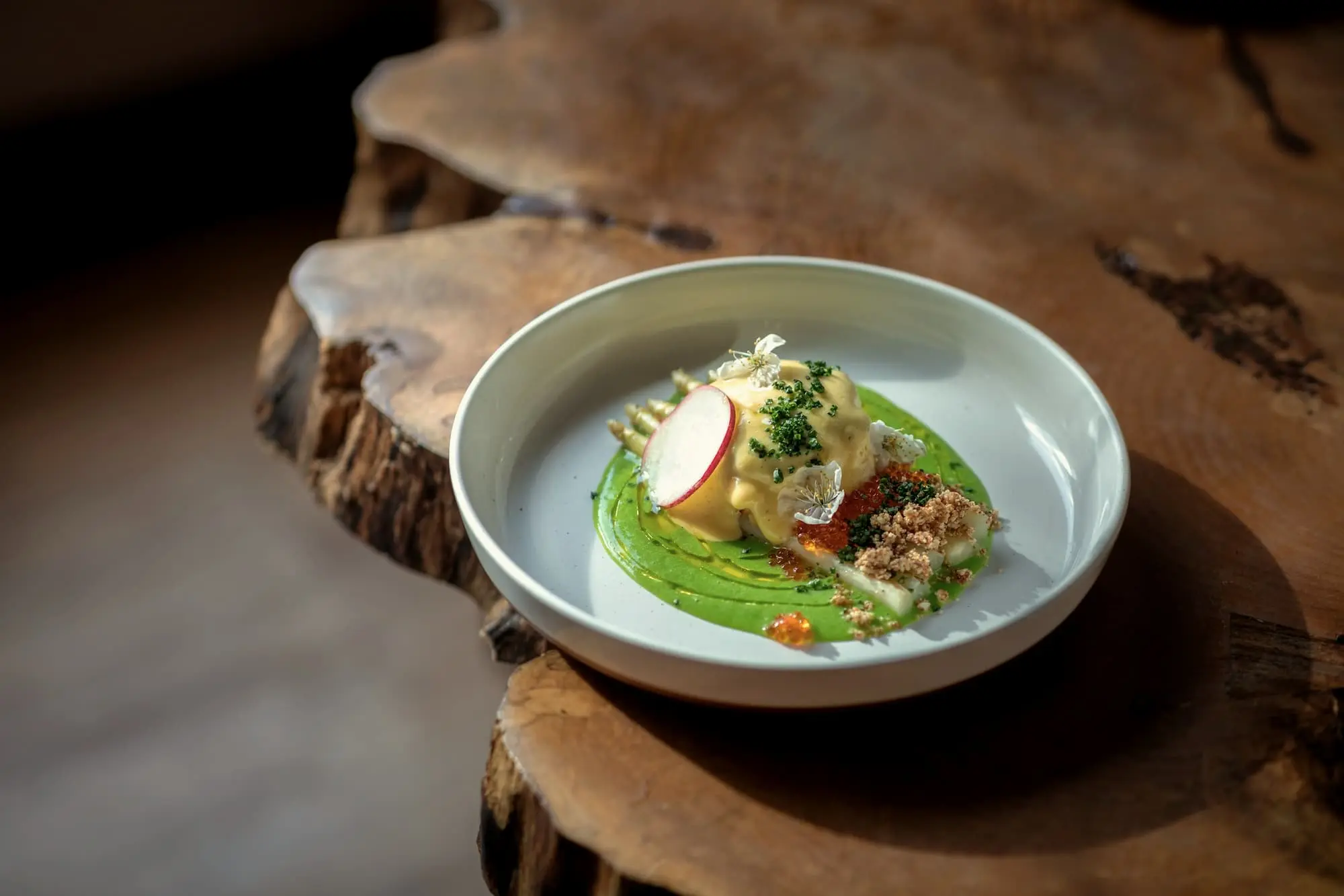A small bowl of green sauce and white fish on a slab of raw timber