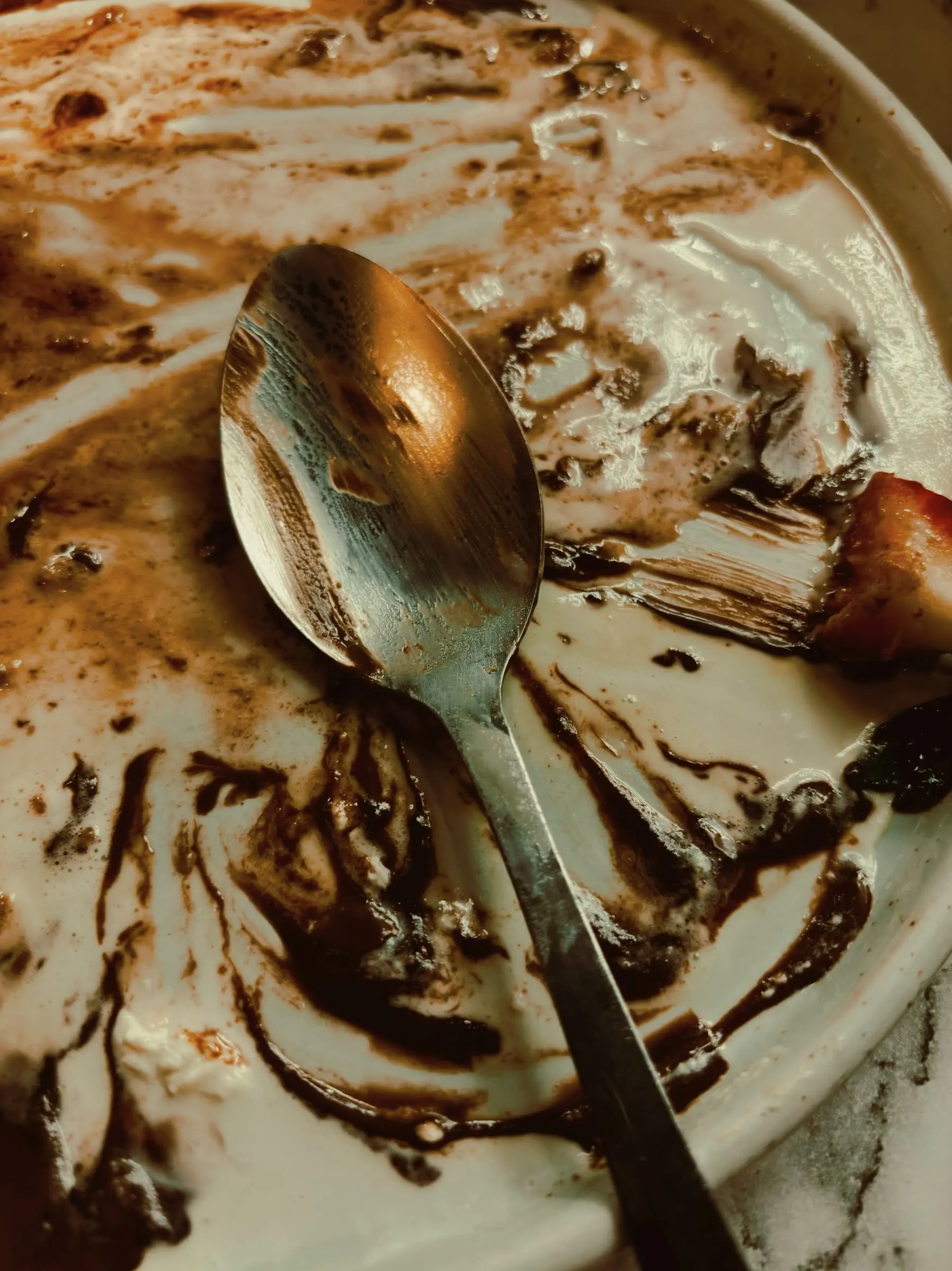 An old spoon on a plate streaked with the remains of a chocolate dessert