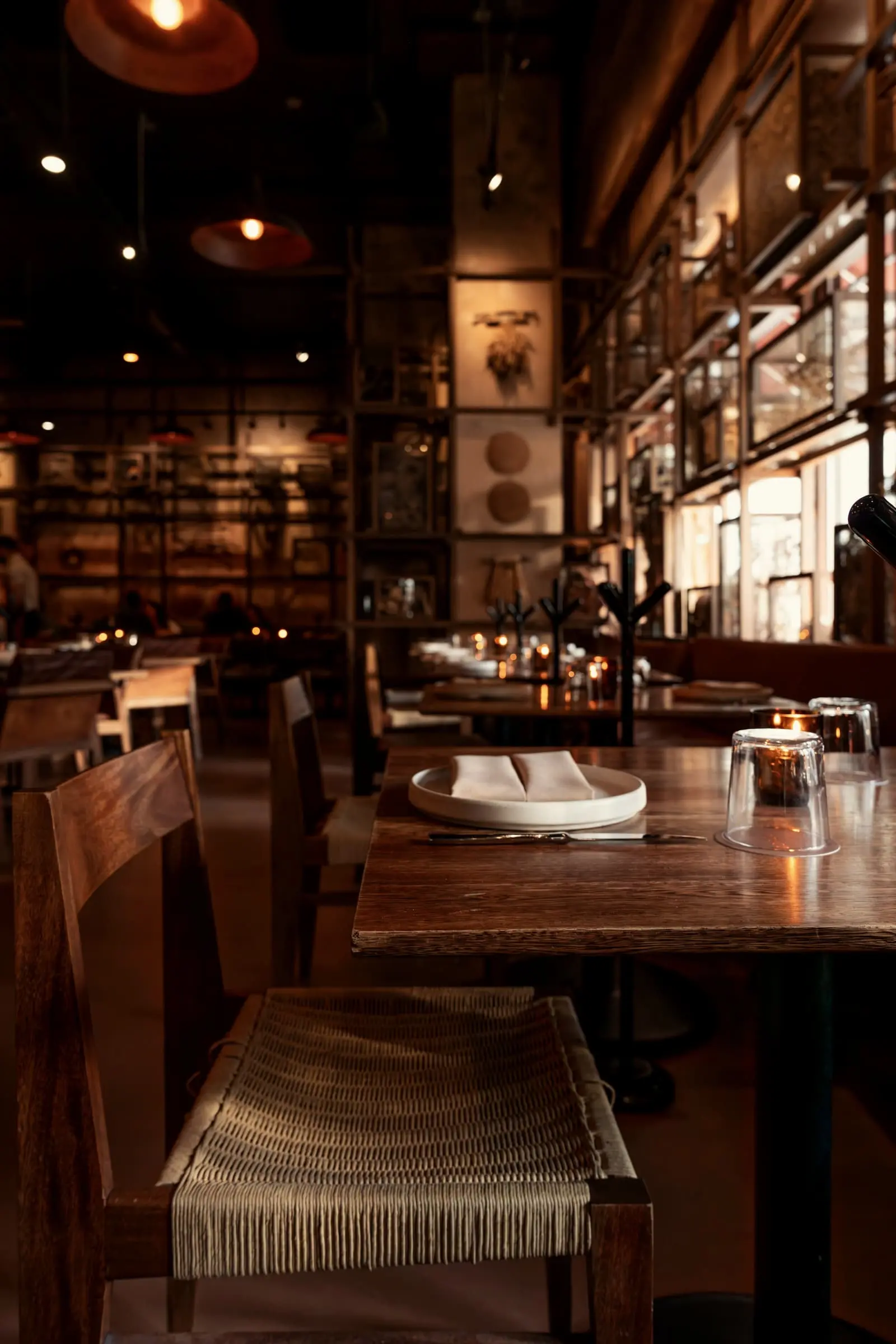 A wooden table in a warm restaurant lined with shelves and low lamps