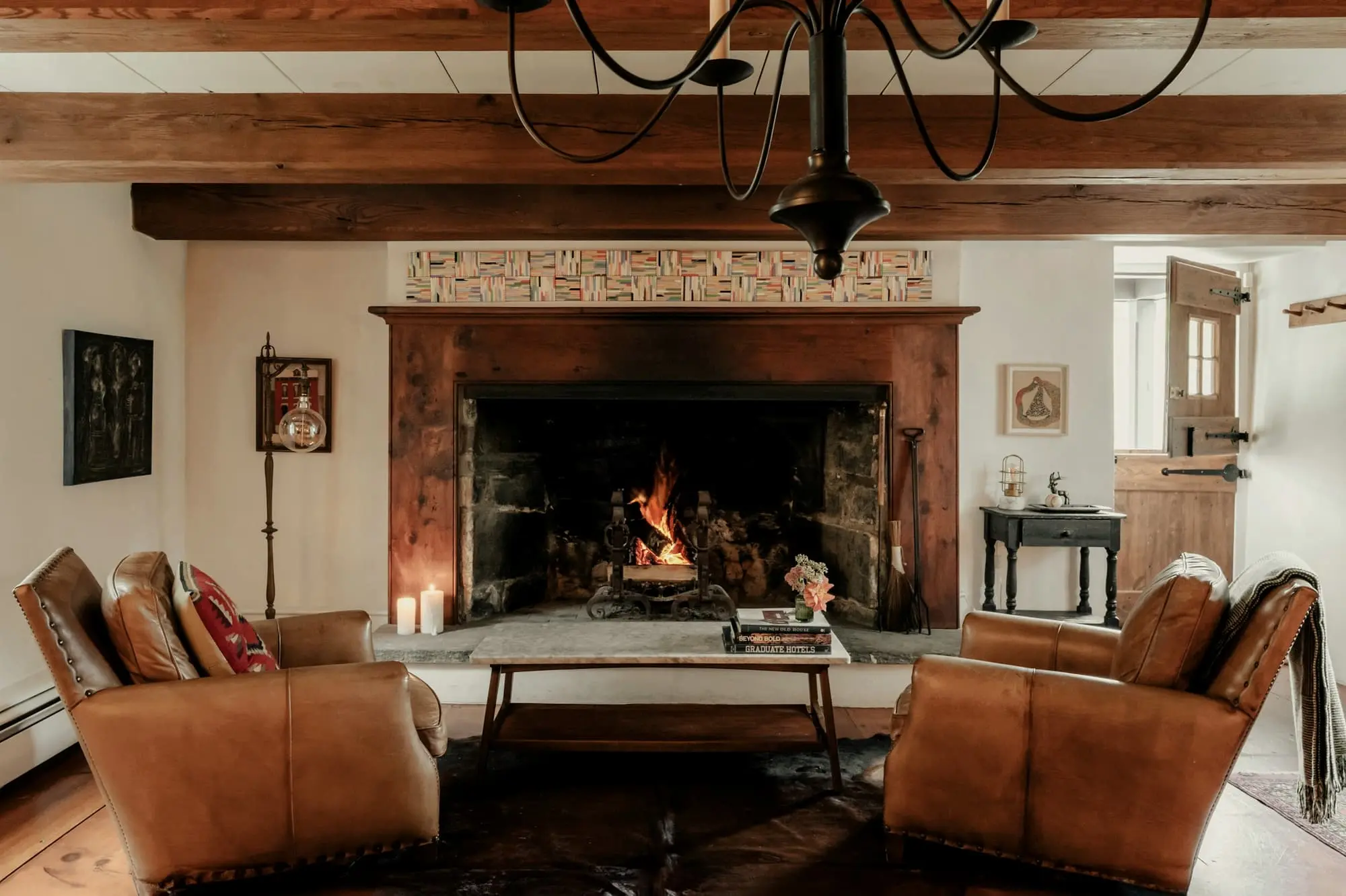 Leather armchairs drawn up to a big brick fireplace beneath a timber beam