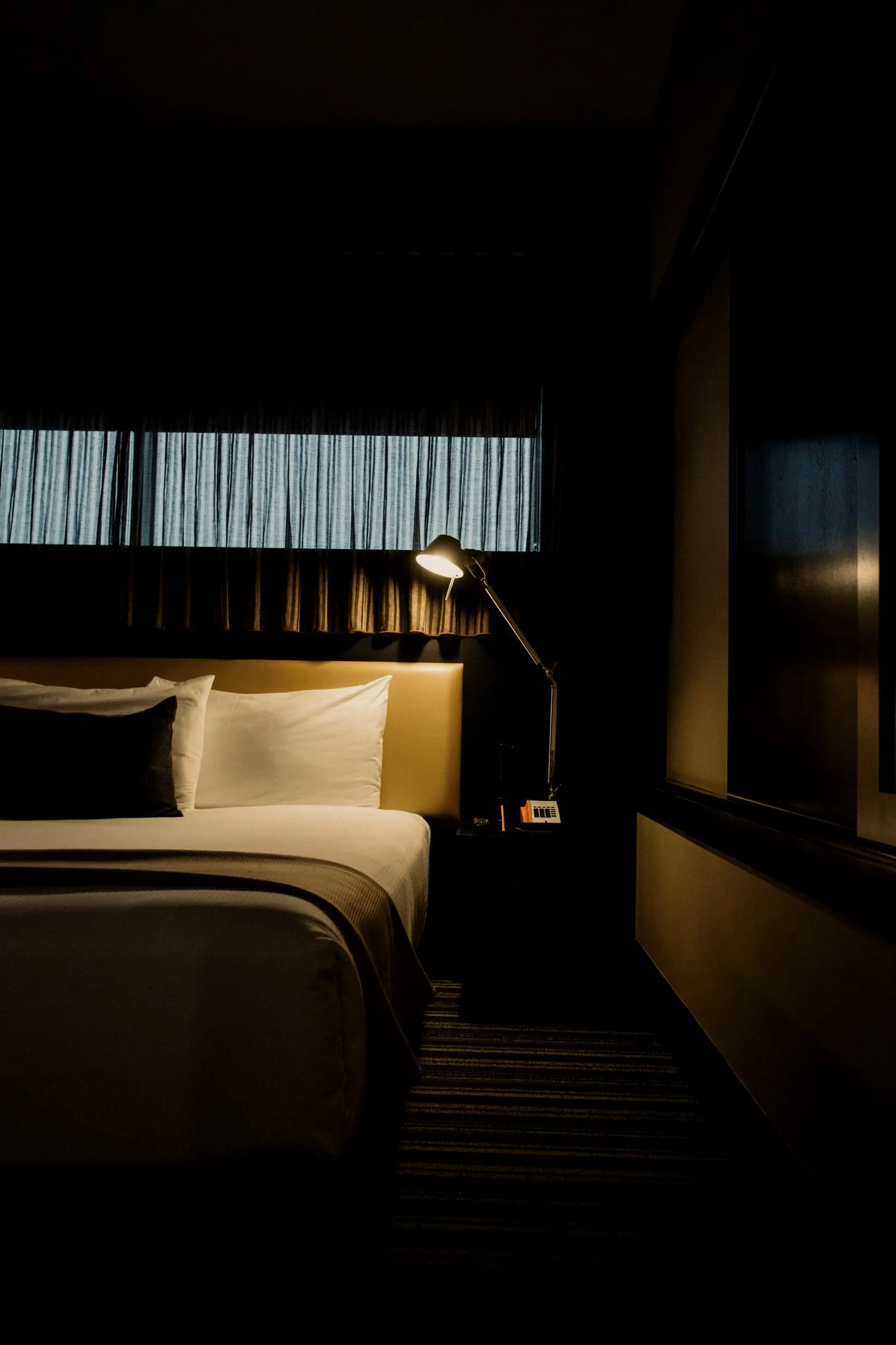 A bed against an amber headboard in a dark room, a slatted window above it