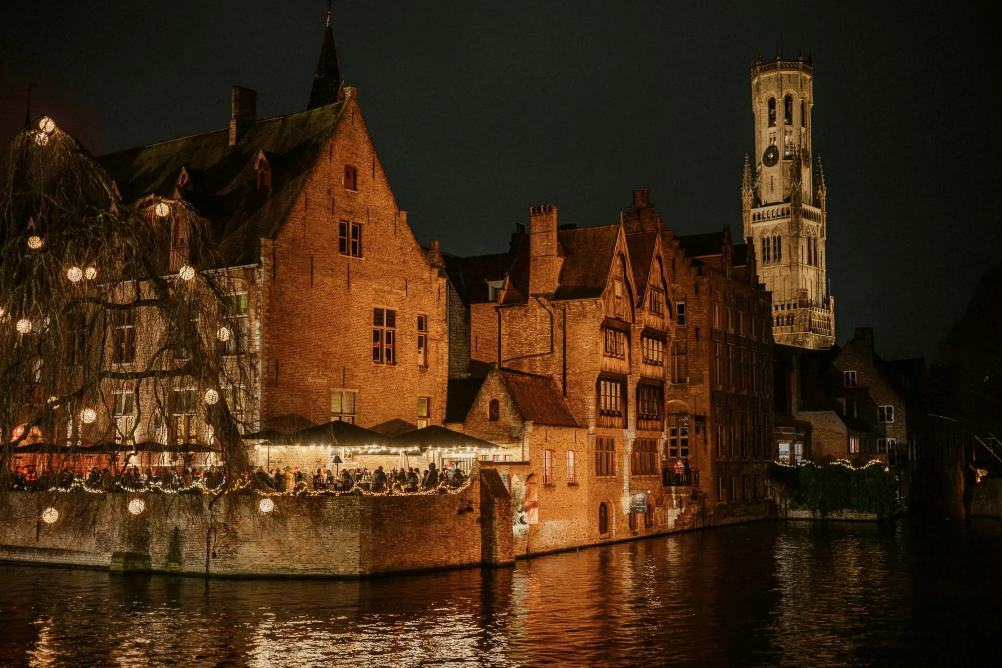Brick gables and a belfry lit up at night above a still canal