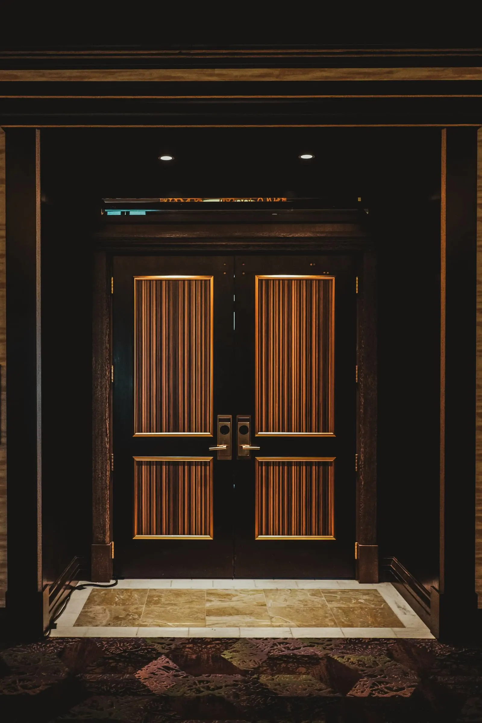 Tall walnut double doors with brass plates at the end of a dark hall