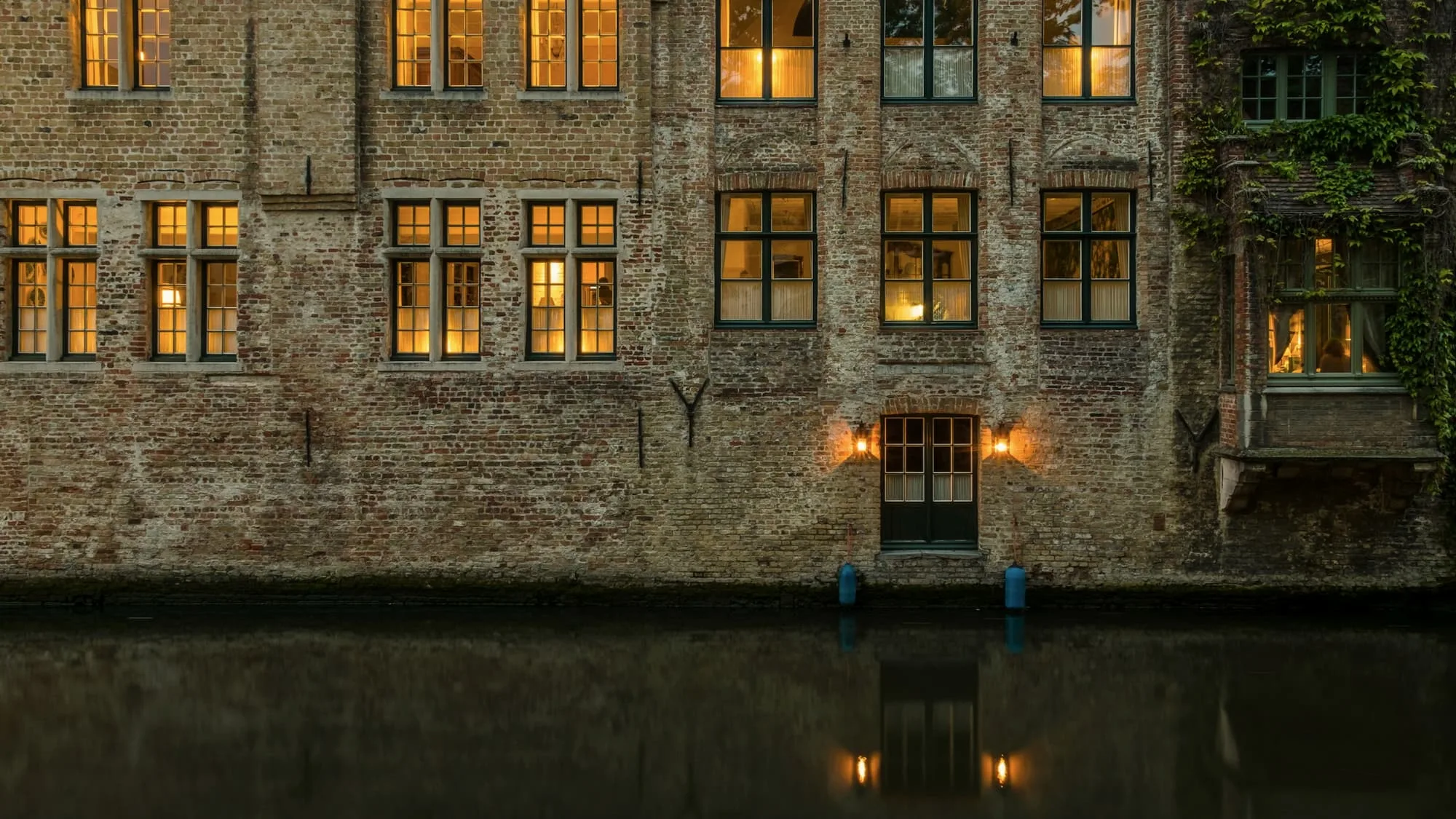 A weathered brick facade with lit windows above dark canal water