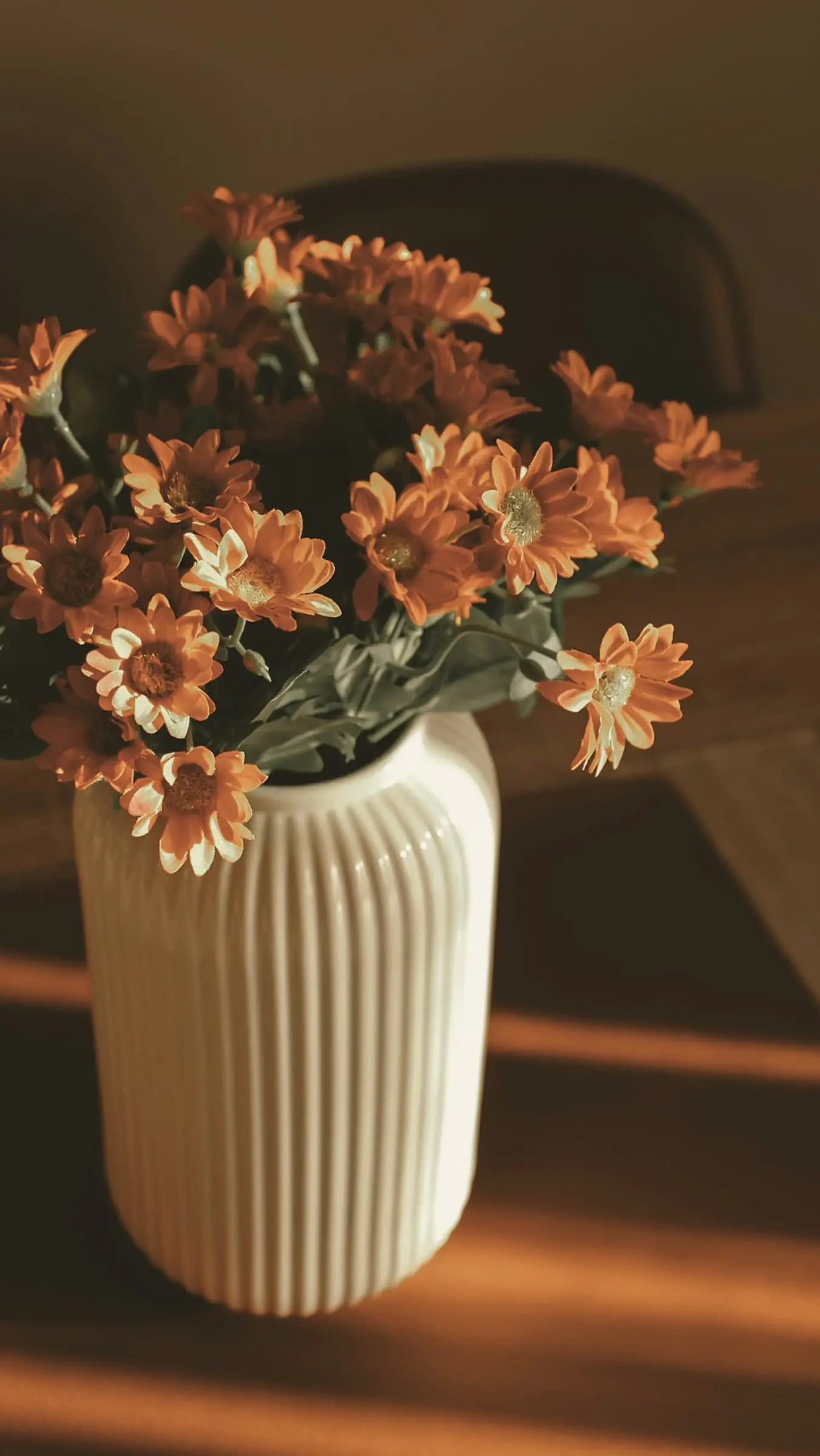 Burnt-orange flowers in a ribbed white vase in late sun