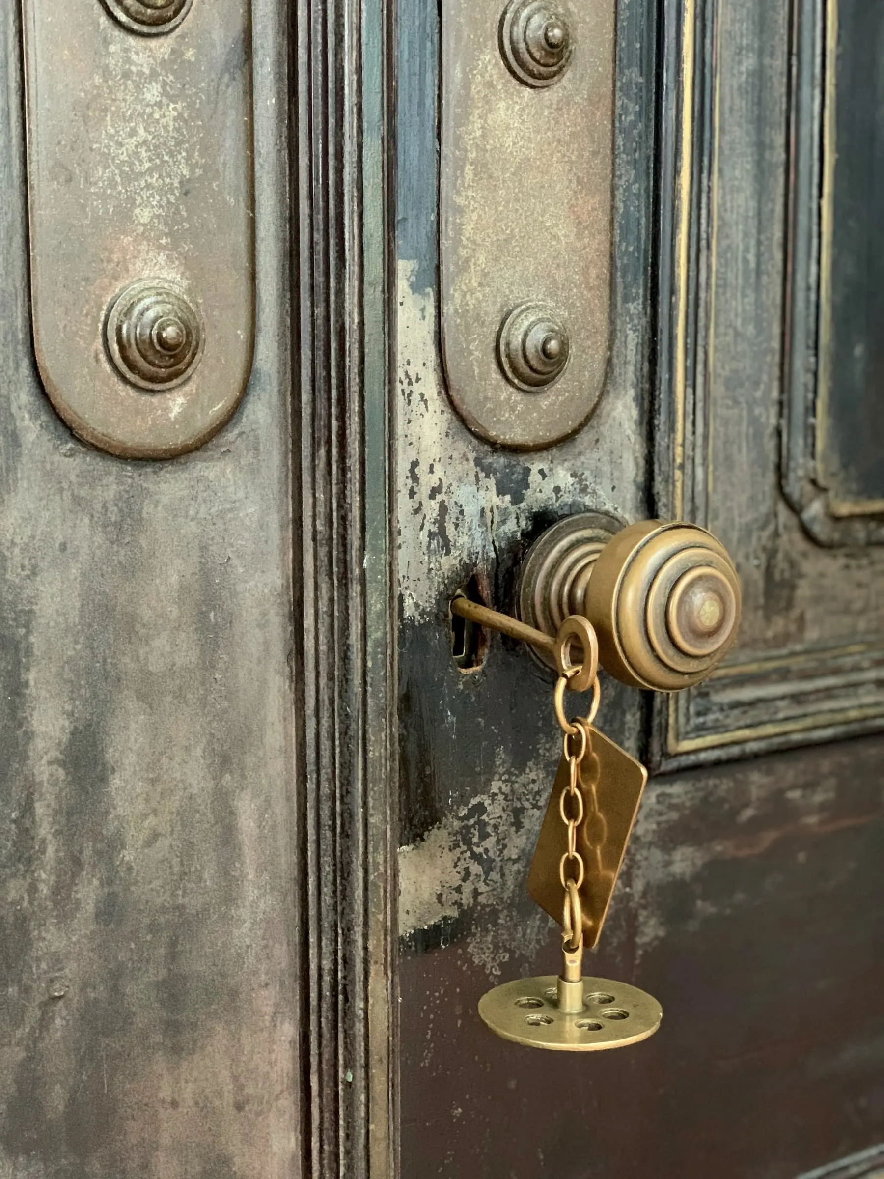 An old key on a brass chain hanging from a door knob on a weathered door