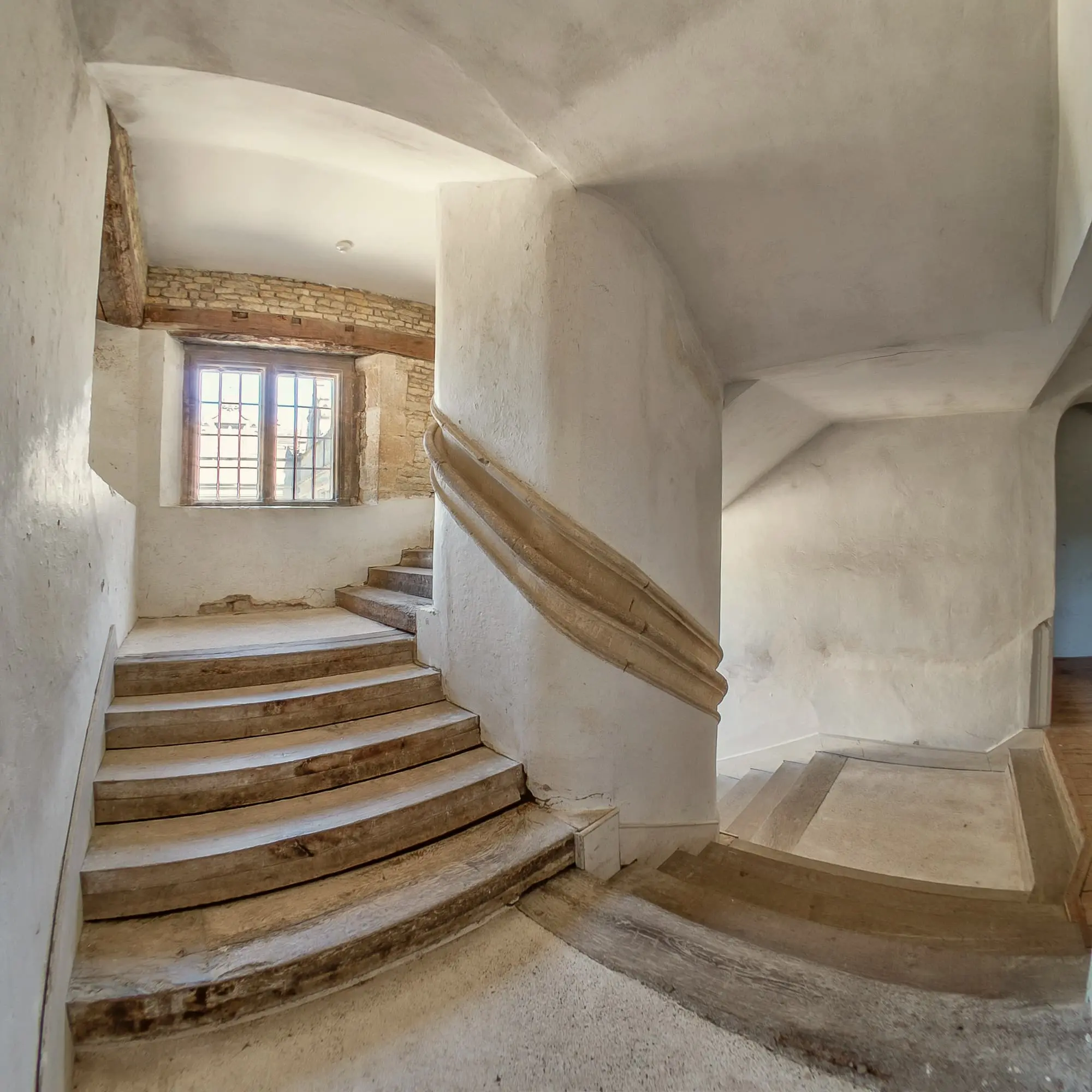 Worn stone stairs turning up a plastered wall towards a small window