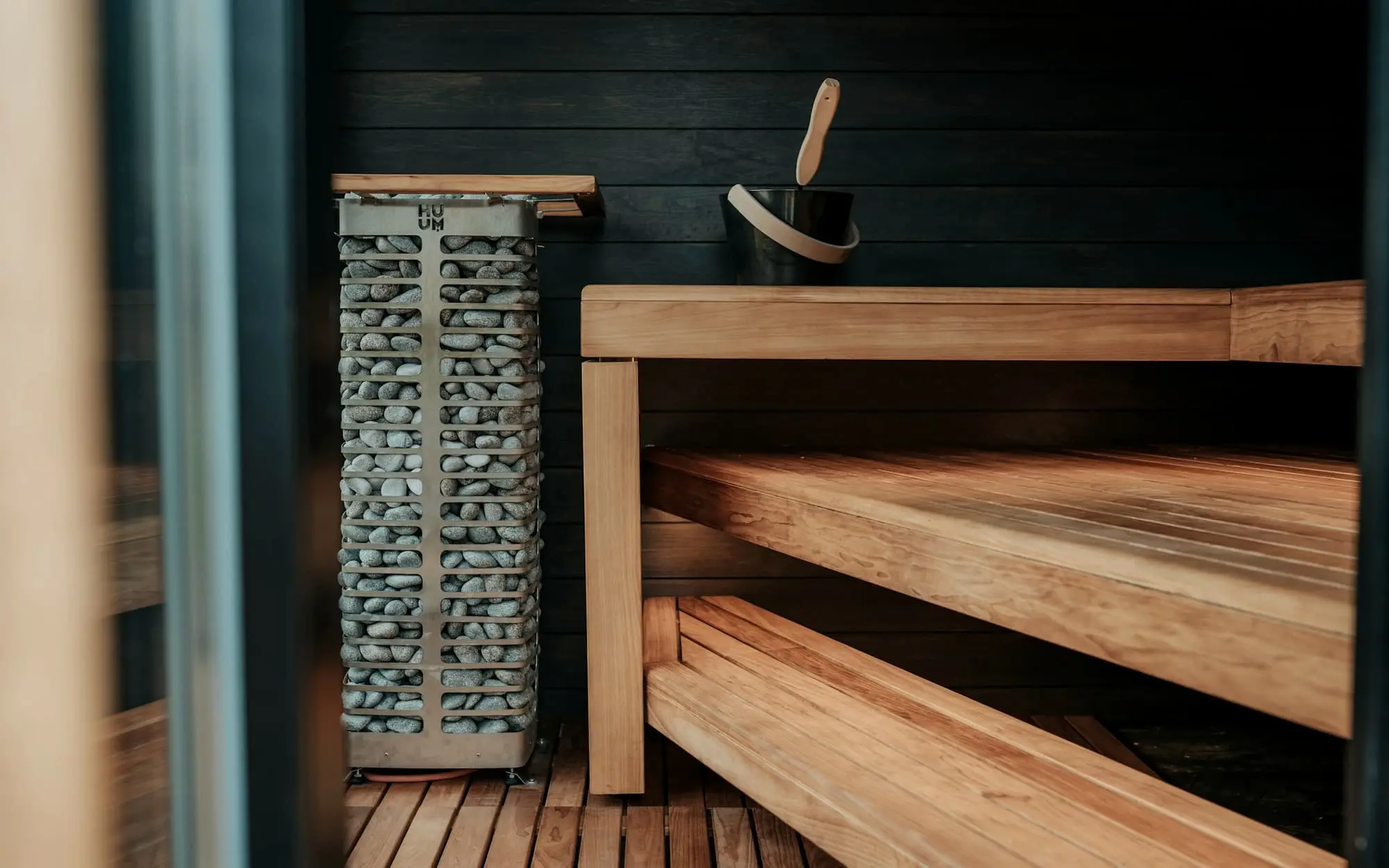 A stone heater and timber benches against a charred black wall