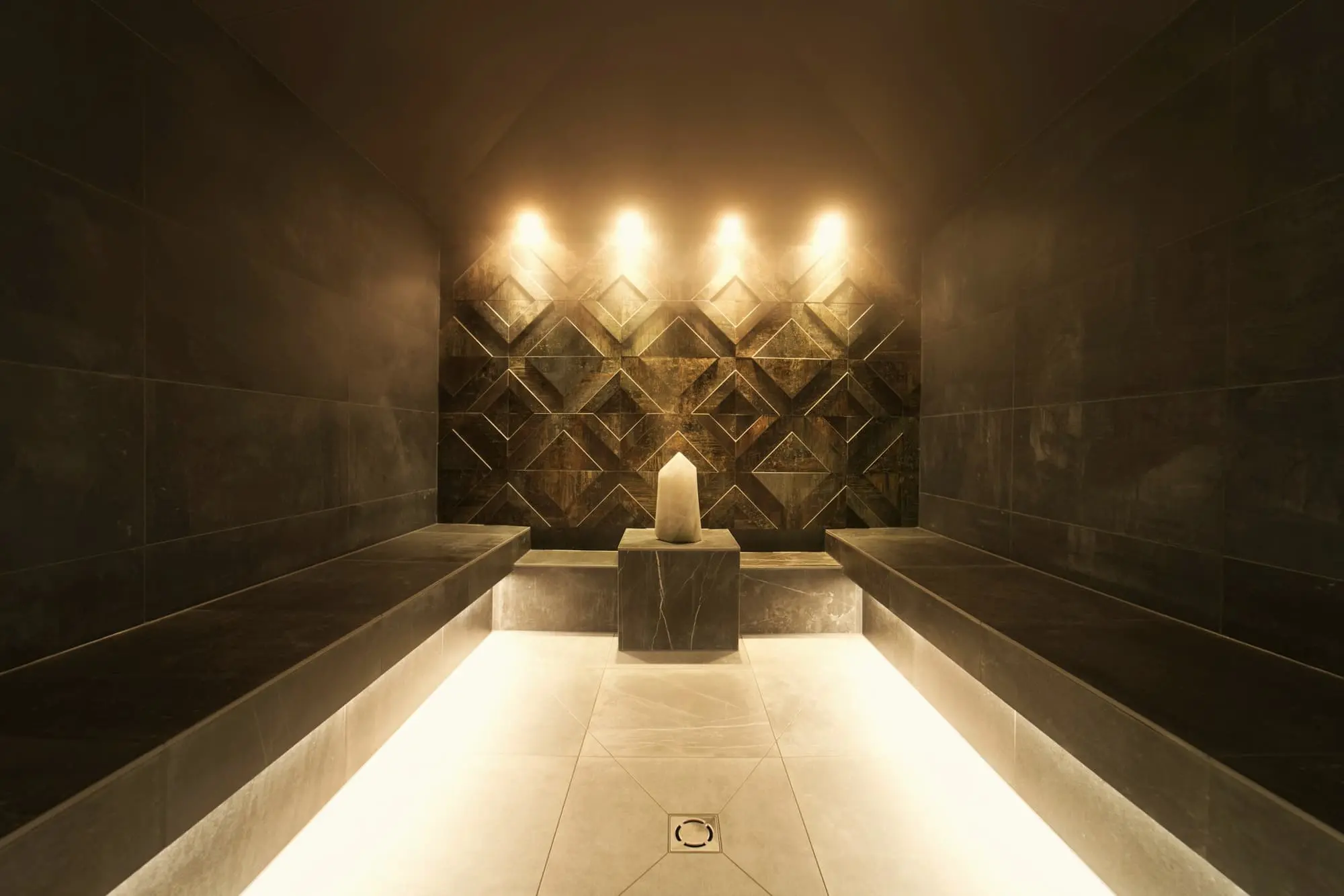 A long pale steam bench leading to a wall of lit candles