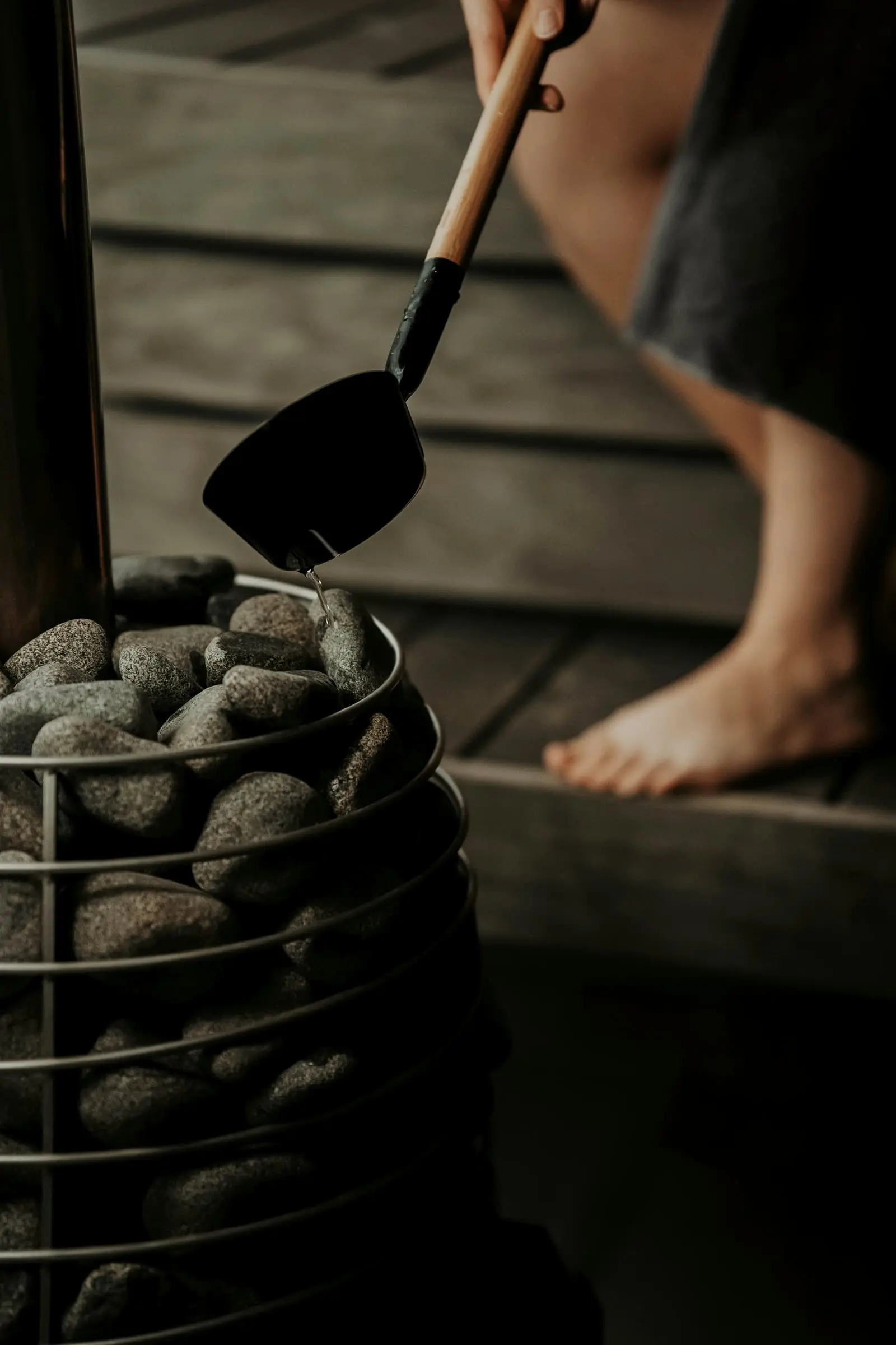 Water being ladled onto sauna stones, a bare foot on the bench above