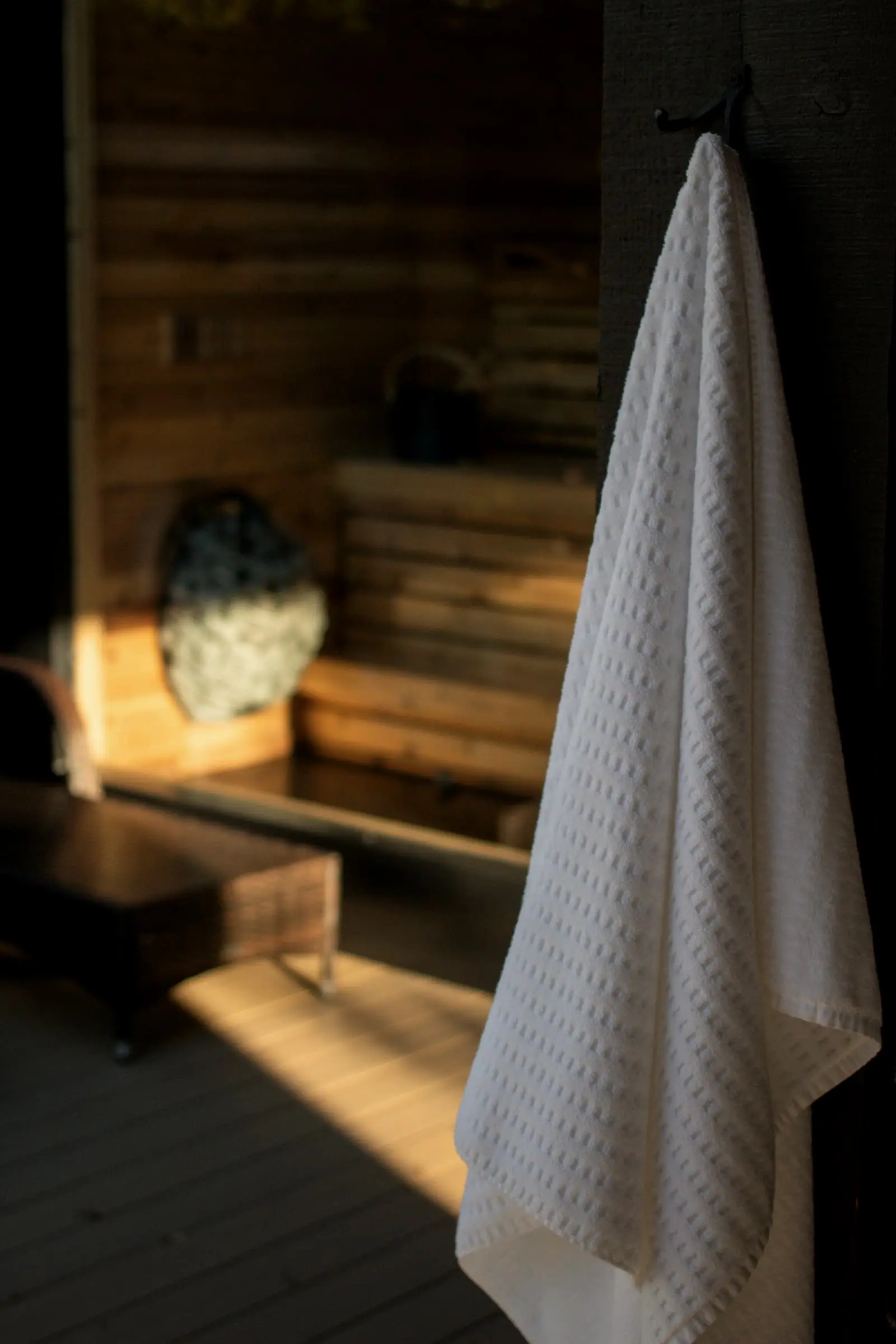 A white towel hanging at the door of a warm timber sauna