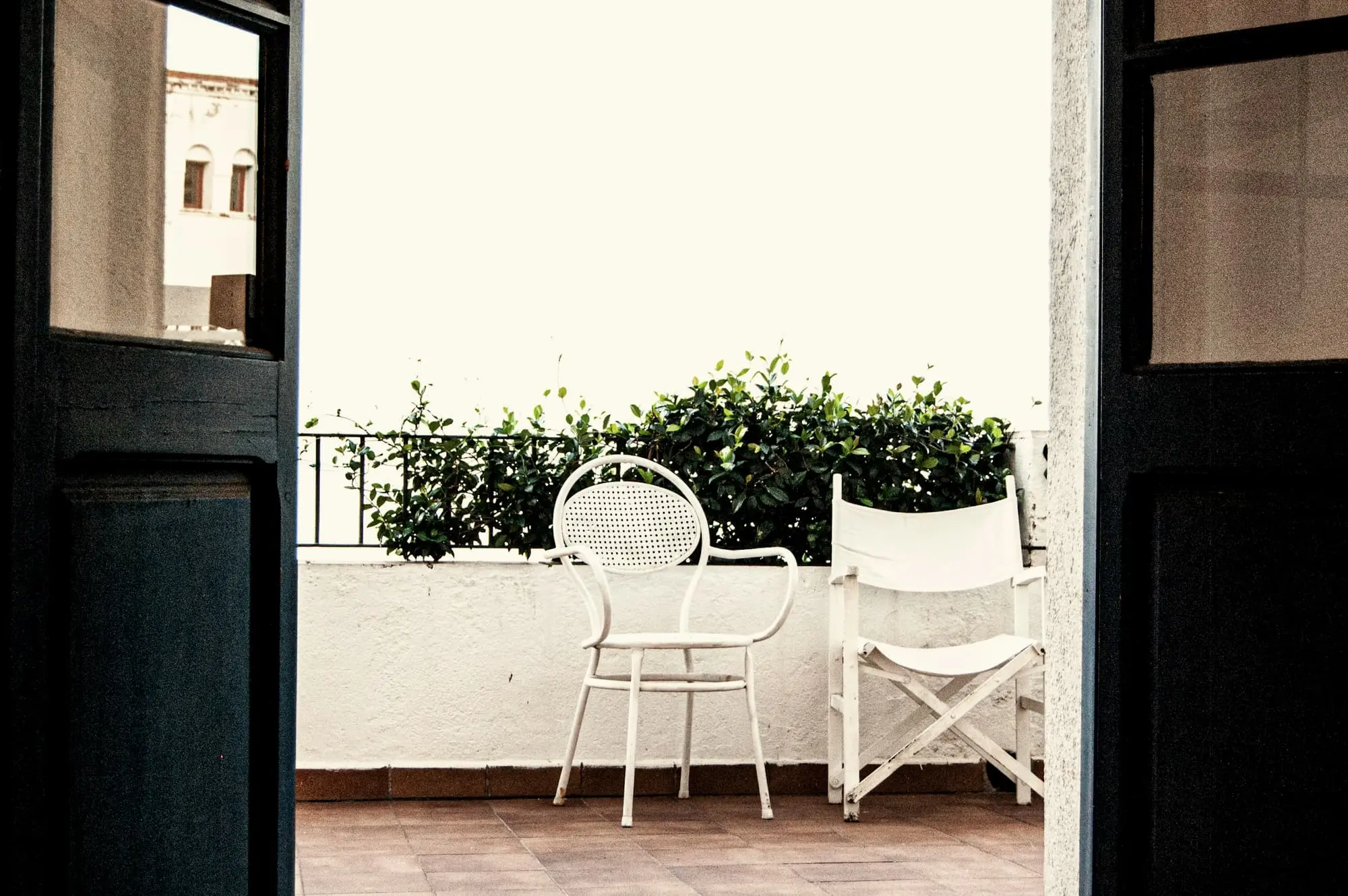 Two chairs on a small terrace seen through dark open doors